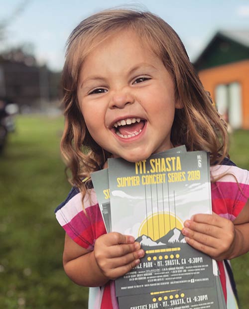 Little girl holding a stack of Mt. Shasta Community Concert Series flyers